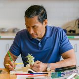 A person holding a plant and drawing with a green colored pencil