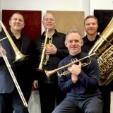 Four men holding brass instruments smile and pose for the camera