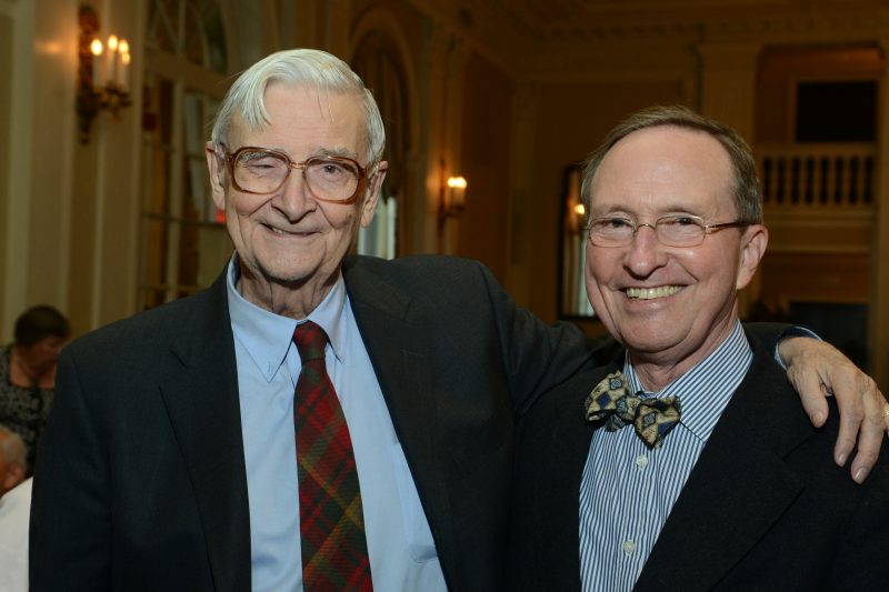 Two men in suits smile as they pose for a photo