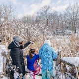 A parent and two children look out over a snowy landscape in NYBG
