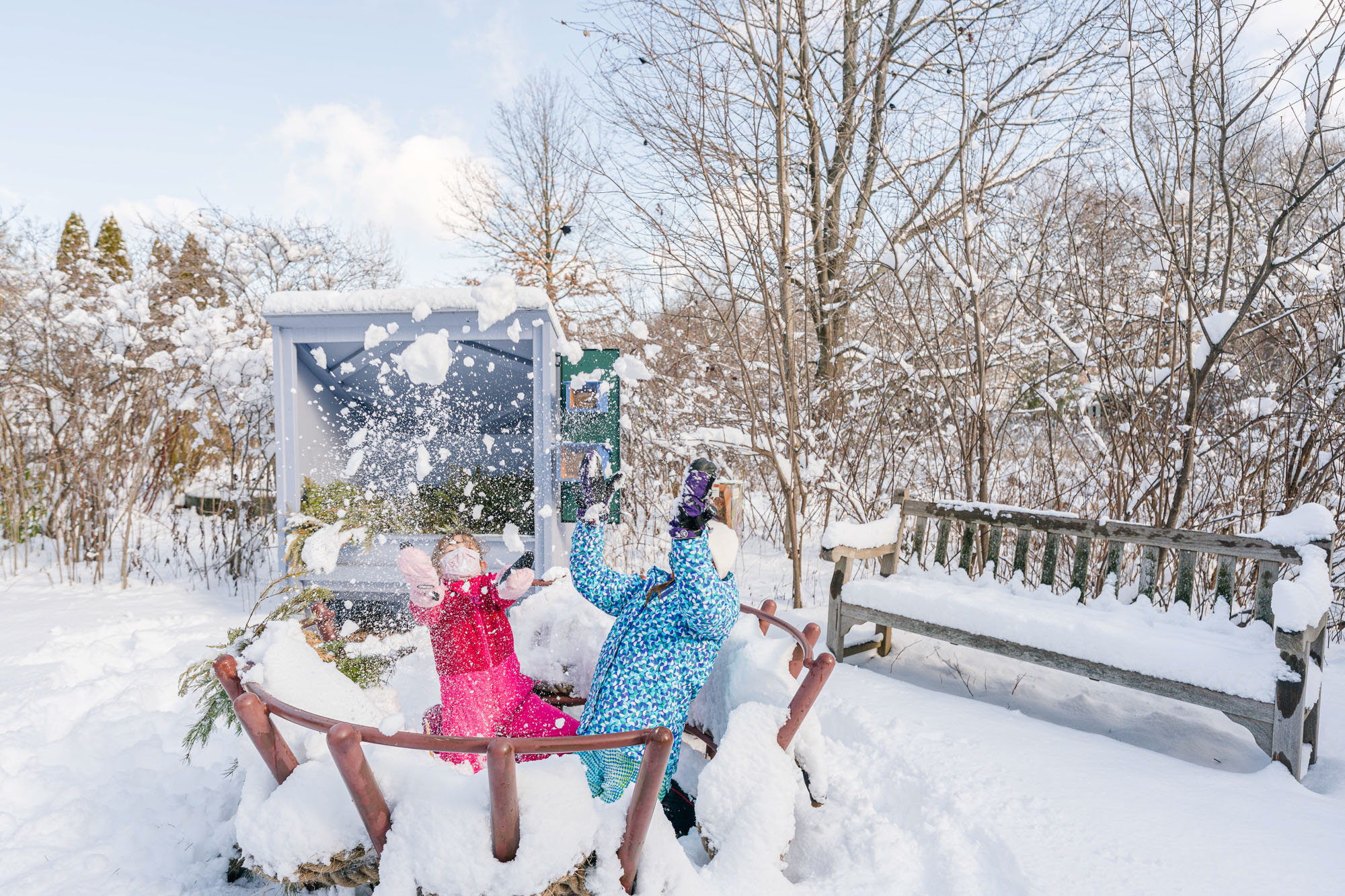 Children in blue and pink parkas throw snow up into the air