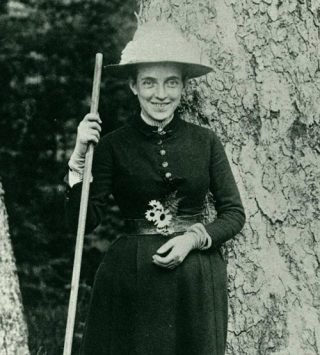 A woman in a dark dress poses for a photo while carrying a walking stick