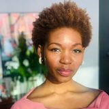 Headshot of Isha Gutierrez-Sumner, wearing a pink shirt in the sunlight