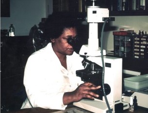 A woman in a white lab coat observes a specimen through a large microscope