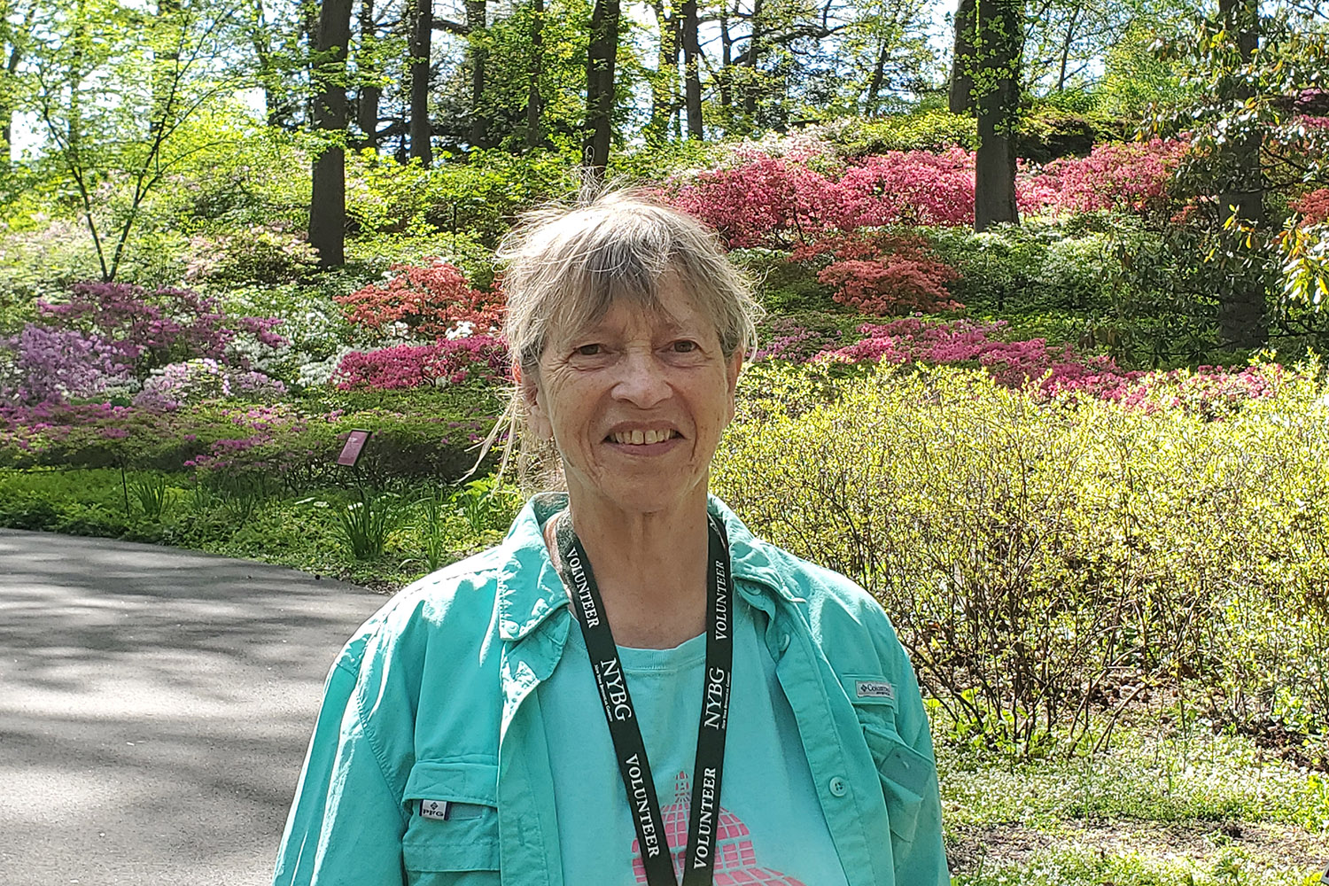 A woman in a sea green shirt poses for a photo in a garden full of pink flowers