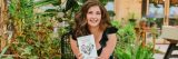 Maria Failla holing her book, Growing Joy, surrounded by plants