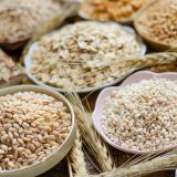 Closed up dry organic pearl barley seed in flower shape ceramic bowl with other brown cereal and grain seed on wooden background.