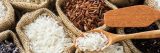 Multiple bags of grains of rice shown, white, red and black with a brown wooden spoon holding some of the white rice in it.