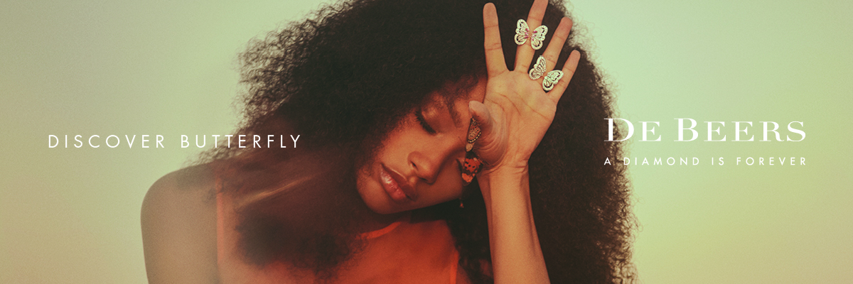 advertisement with woman with brown curly hair with hand to forehead displaying gold butterfly rings on fingers blurred background Discover Butterflies DeBeers logo A diamond is forever