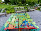 picnic table painted with images of people and a garden scene