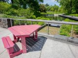 deep red picnic table on a walkway in front of a railing in front of a garden with a large water feature