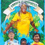 Mural by Bronx-based artist André Trenier, illustrating a colorful mural in blues, yellows, and greens , depicting a woman with long gray dreadlocks, arms opened and lips upturned. Three additional people in colorful clothing are arrayed beneath her, working with fruits and vegetables. It says 