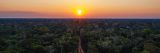 A photo taken from high above a tropical forest of green trees, stretching out to the horizon where the sun is just about to set