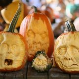 three large orange pumpkins and one small green pumpkin carved with spooky faces