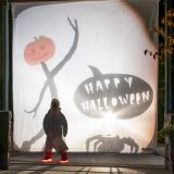 a child looking at shadow puppets of a jack-o-lantern figure and a pumpkin that says "Happy Halloween"