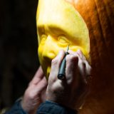 a person carving out a human eye on an orange pumpkin