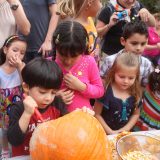 several children crowded around a child carving a pumpkin on a table