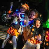 A parent with two children, all dressed in Halloween costumes, hug while posing for a photo at night