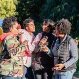 A group of people in light fall jackets gather around to share cups of beer