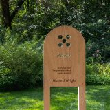 A wooden sign displaying poetry sits in a sunny green outdoor space