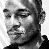 A black and white photo of a man with short hair and a black shirt posing for a photo