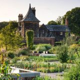 A classical manor sits among sprawling green gardens on a sunny day