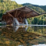 A unique series of roofed outdoor structures butts up against a shallow water feature in nature