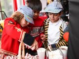 Three children in train conductor hats, one pouring whip cream into a white cup with tiny white marshmellows in a clear containter. There are red and white stripped candy canes in a basket.