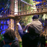 A couple explore the Holiday Train Show after dark, showing their child one of the bridges that passes over head