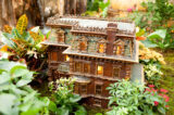 A three-story building with a green roof and warmly lit resin windows, all made from dried plant parts