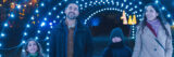 a family of two adults and two children walks down a path and looks up at the light arch they are walking under