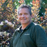 A person with short gray hair and a green shirt poses for a photo outdoors