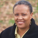 A person with short hair in a black fleece poses outdoors for a photo