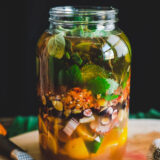A clear glass jar filled with liquid and chopped fruits and vegetables
