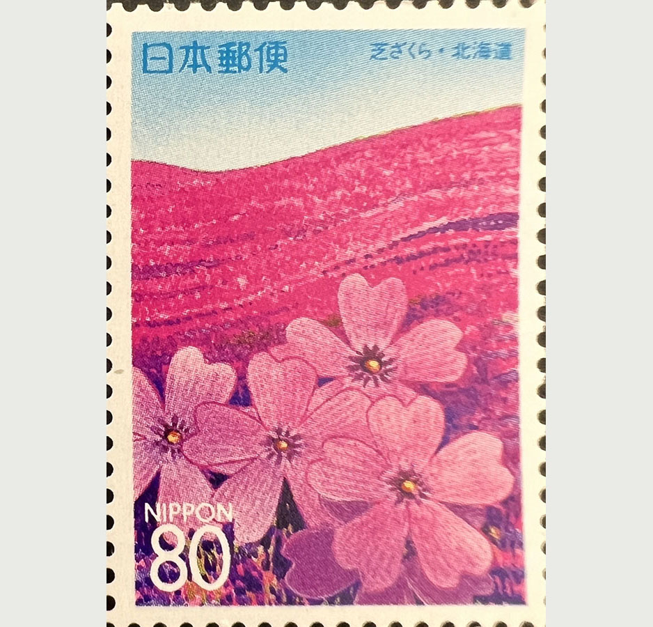 A bright pink postage stamp depicting pink flowers on a hillside