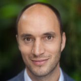 A close-up portrait of author Alexandre Antonelli, softly smiling at the camera.