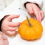 a young person's hands around a small orange pumpkin on a white table