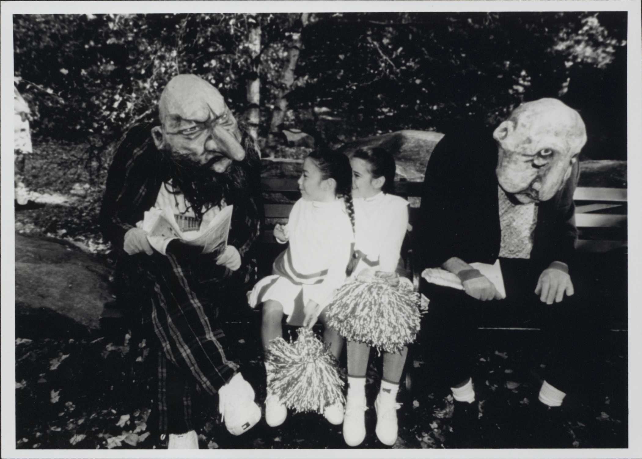 A black and white photo of twins dressed as cheerleaders, sitting between two people in handmade troll costumes