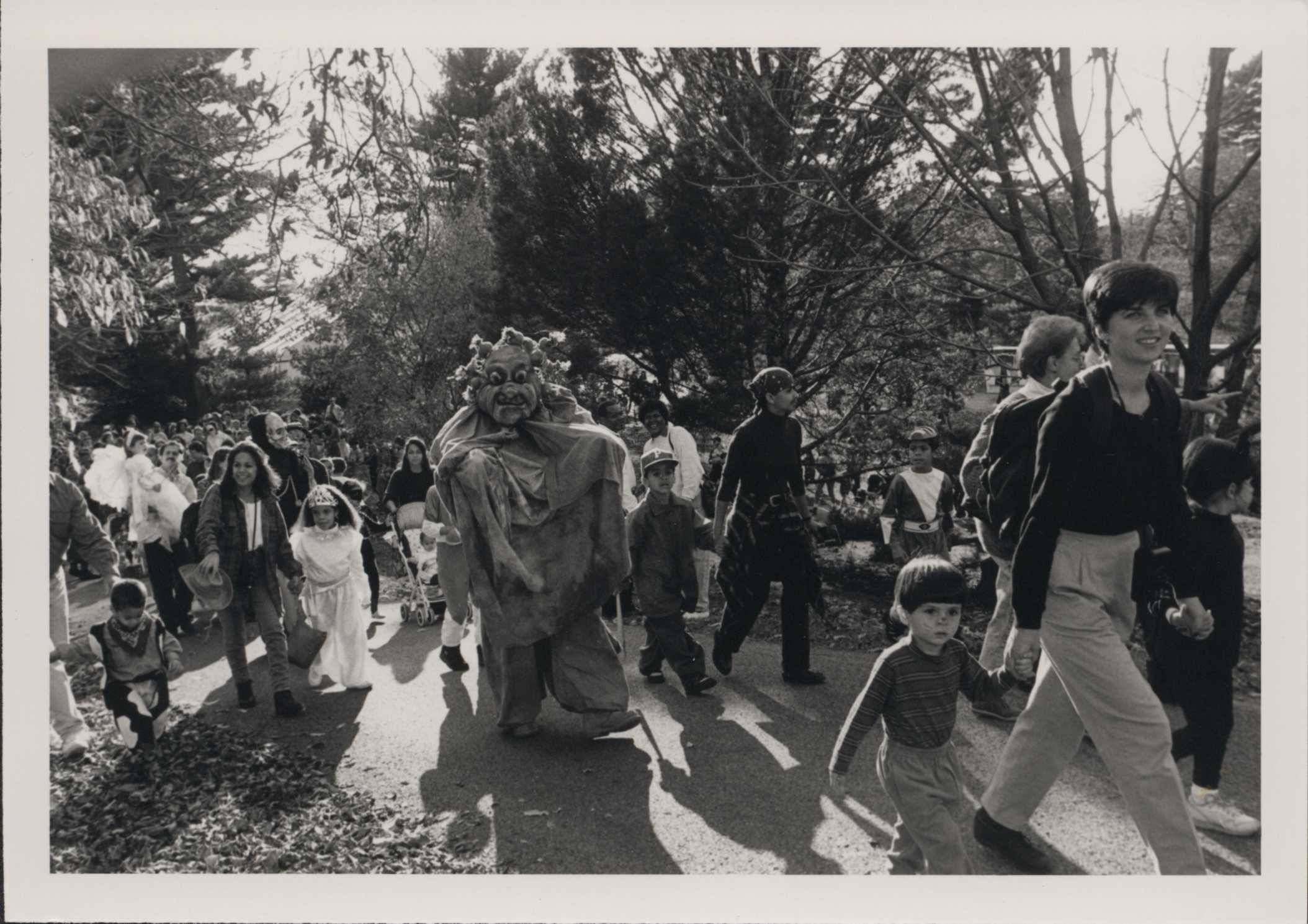 A group of costumed kids and families march on parade in black and white