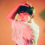 a person in soft orange lighting looking over their shoulder in a white lace top