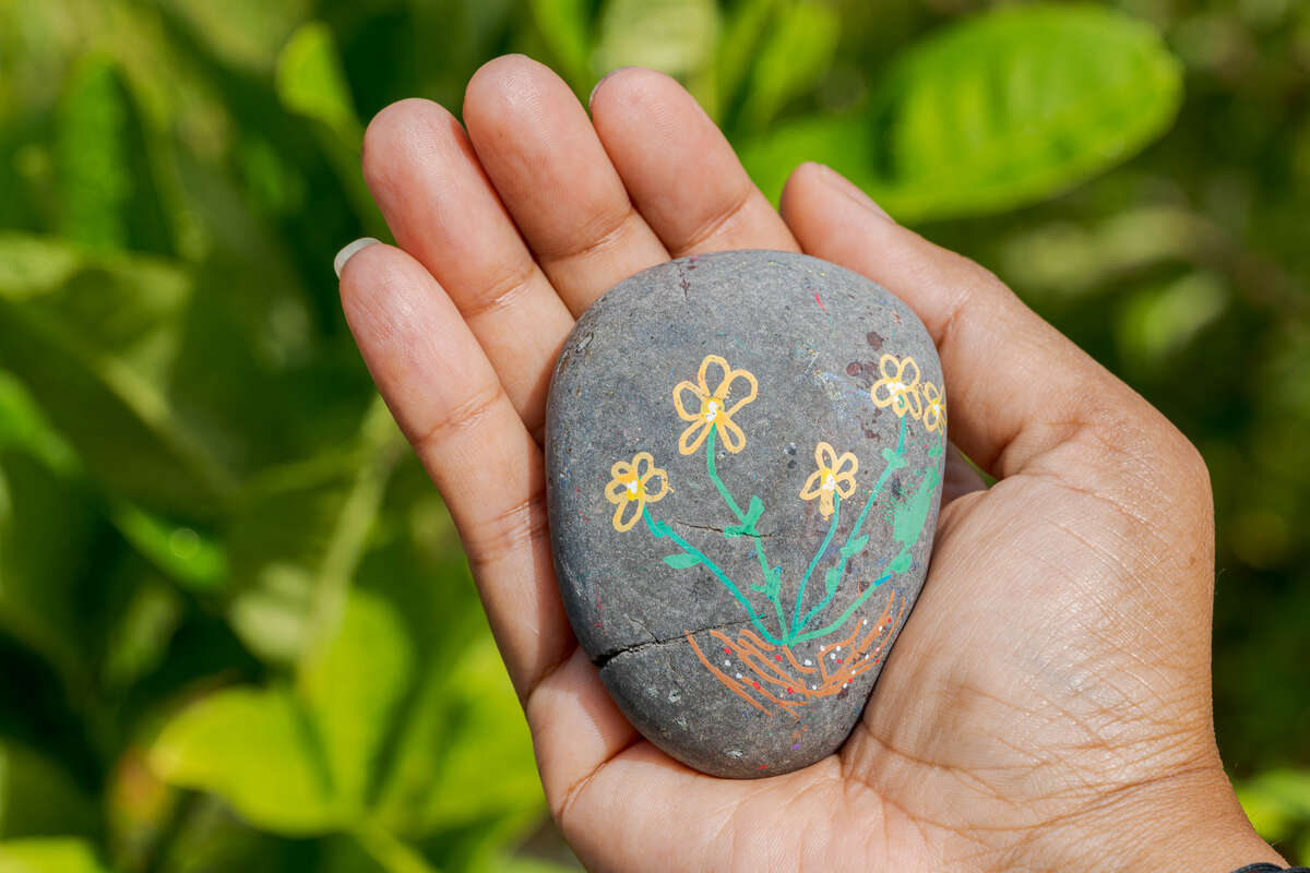 A painted gray rock with yellow and green flowers on it