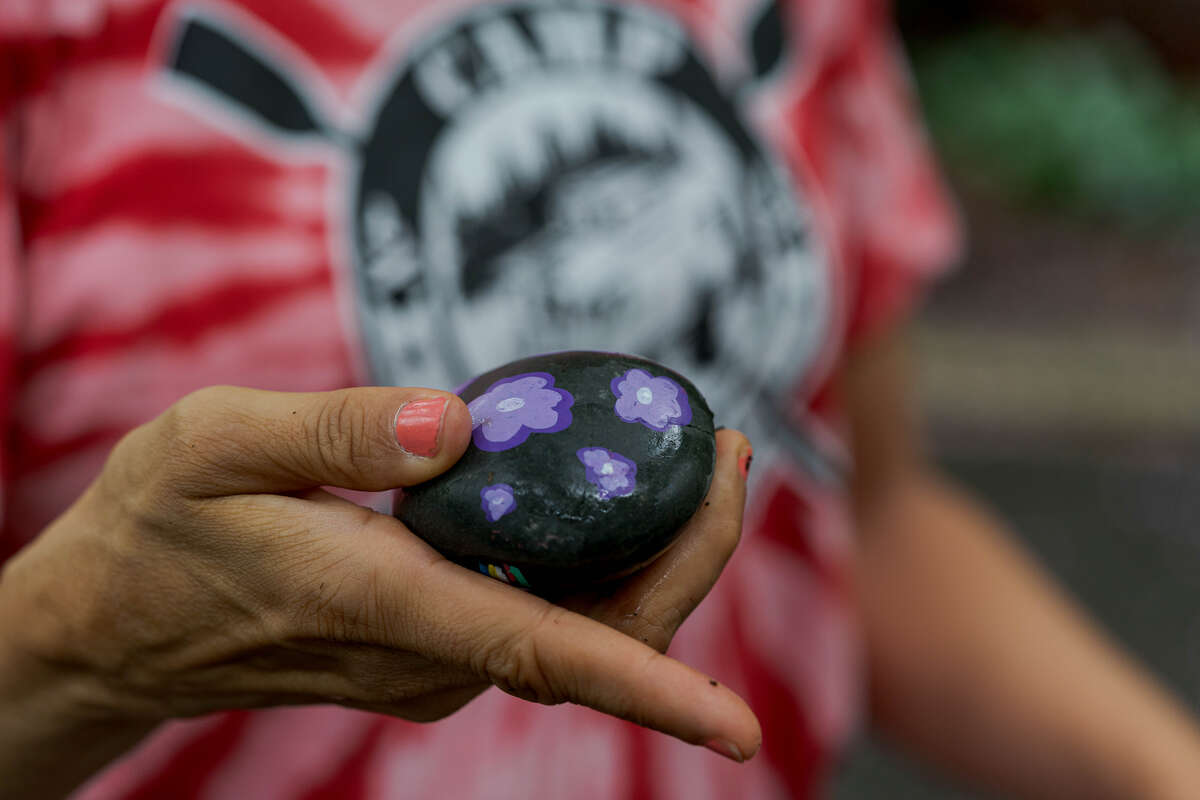 A painted black rock with purple and white flowers on it