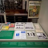 Multiple pages of old pictures and information laid out on display in a case with a green board and informational text about the display.