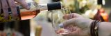 Rosé wine is poured into a short glass, held by someone with white nail polish and bracelets.