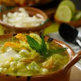 A bowl of steaming hot soup garnished with squash blossoms and green herbs