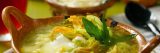 A bowl of steaming soup garnished with yellow squash blossoms and green herbs