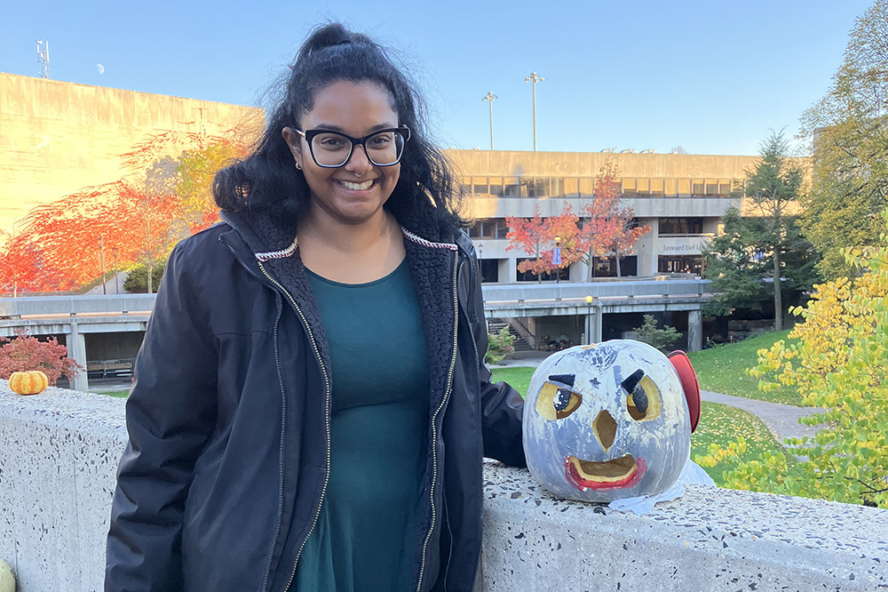 A person in a navy hoodie and green shirt poses with a blue, white, and orange decorated pumpkin