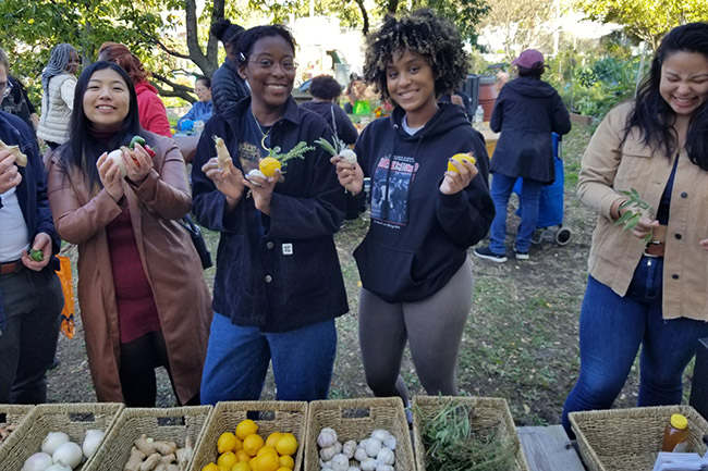 People in warm fall clothing hold up fruits and vegetables as they choose from baskets full of ingredients