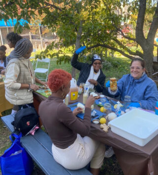 A group of people prepare fruits and vegetables while gathered around a picnic table