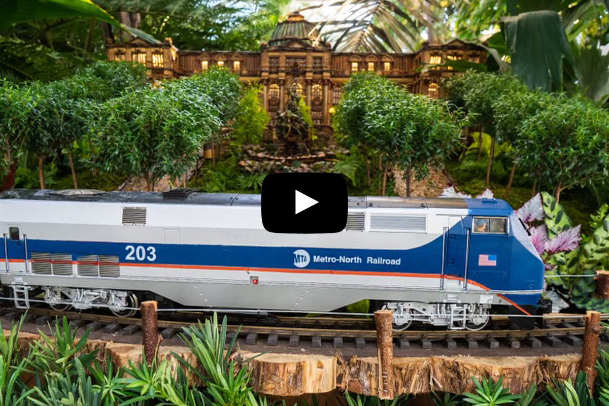 A Metro-North miniature train on the track zipping by a miniature NYBG Library